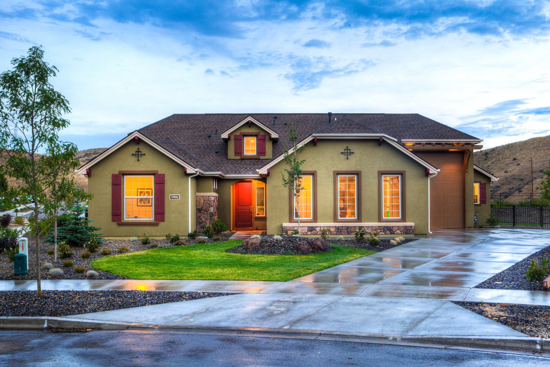 Modern single-story house with lit windows and wet driveway at dusk