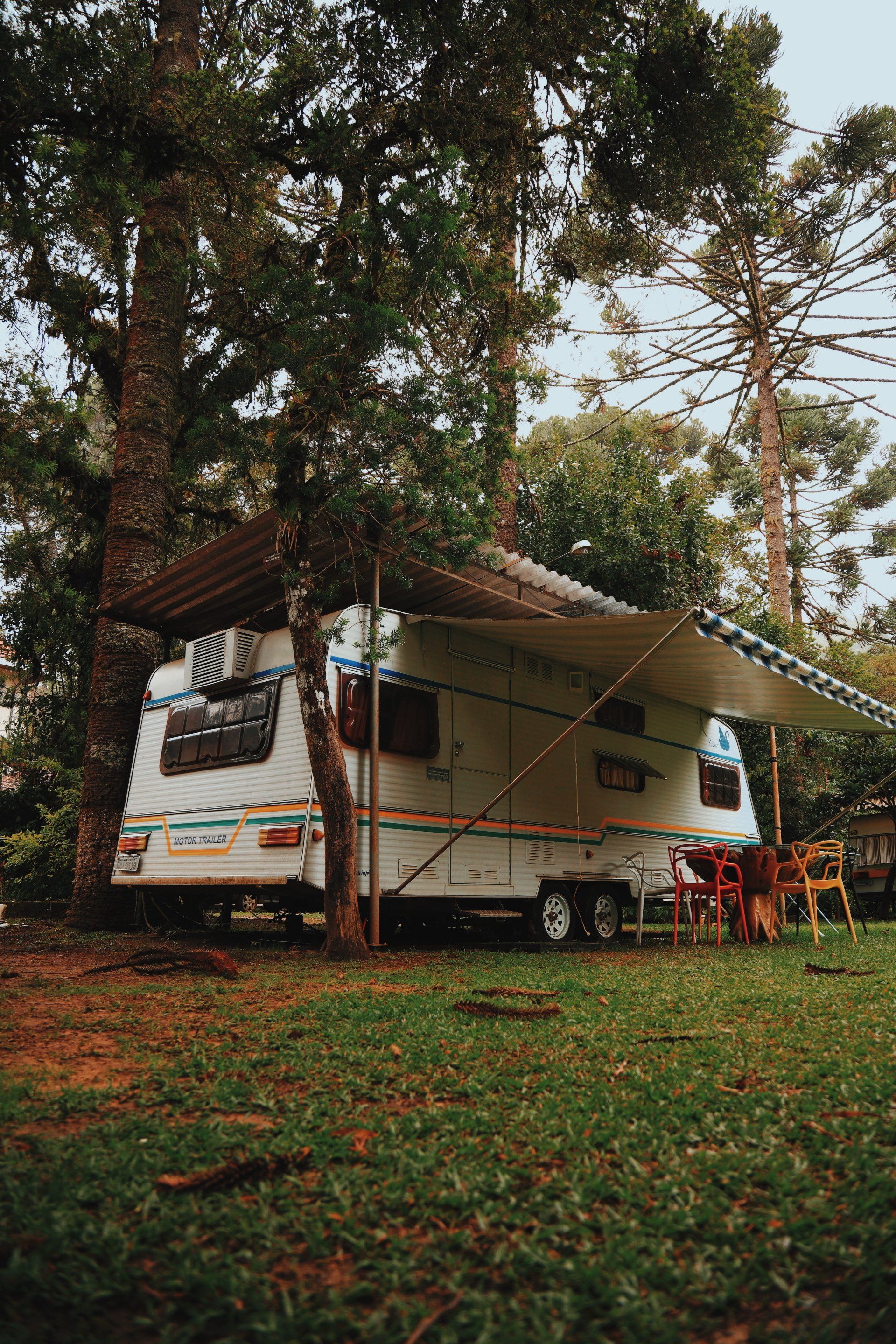White camper van parked under trees with an extended awning in a grassy campsite