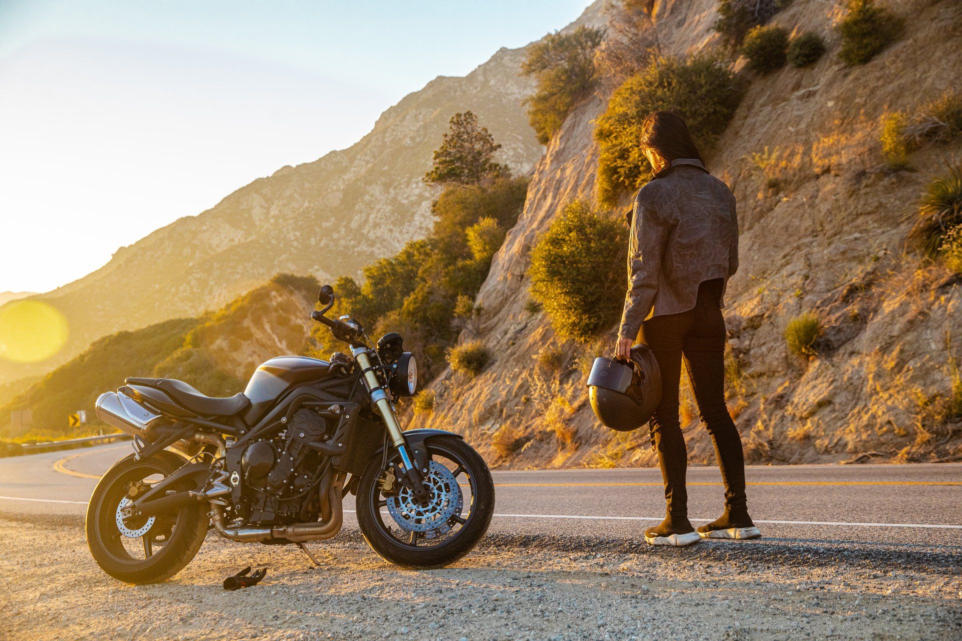 Motorcycle parked on a mountain road beside a person at sunset