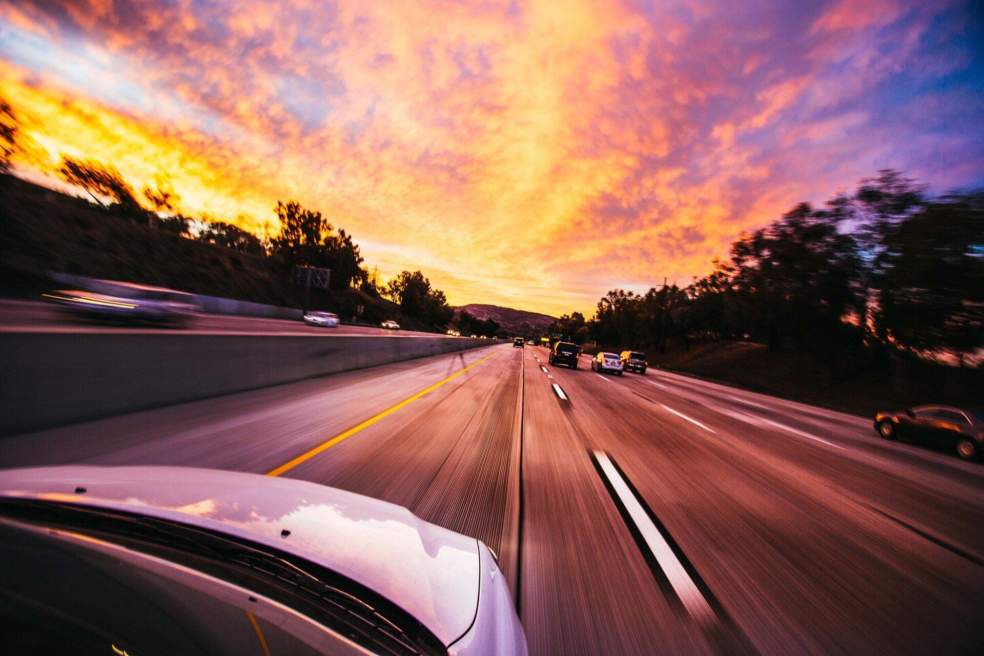 Driving on a highway at sunset, with blurred lanes and a vivid orange-purple sky